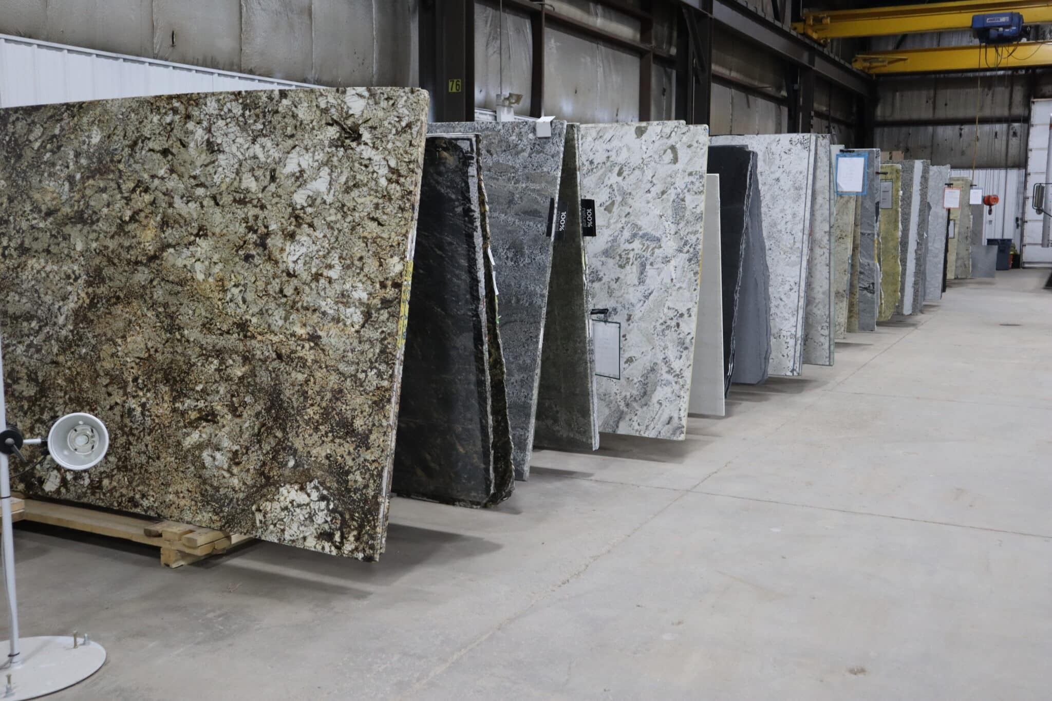 Large stone slabs in various colors and patterns are lined up vertically inside the LouAda Showroom with concrete floors and metal walls.